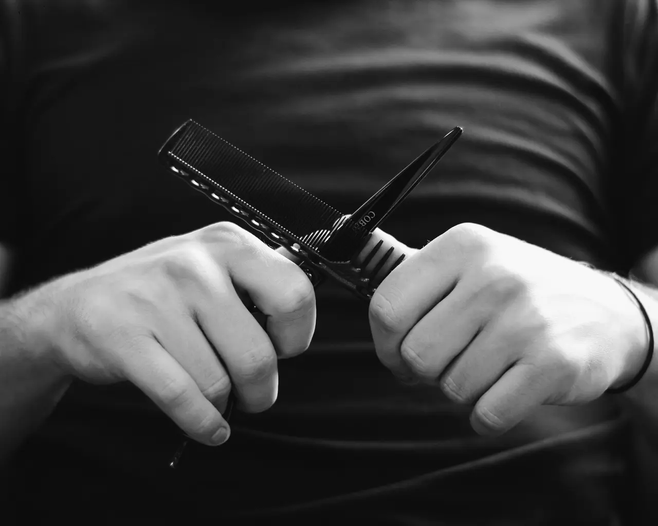 Ciseaux et peigne dans une main, en noir et blanc.