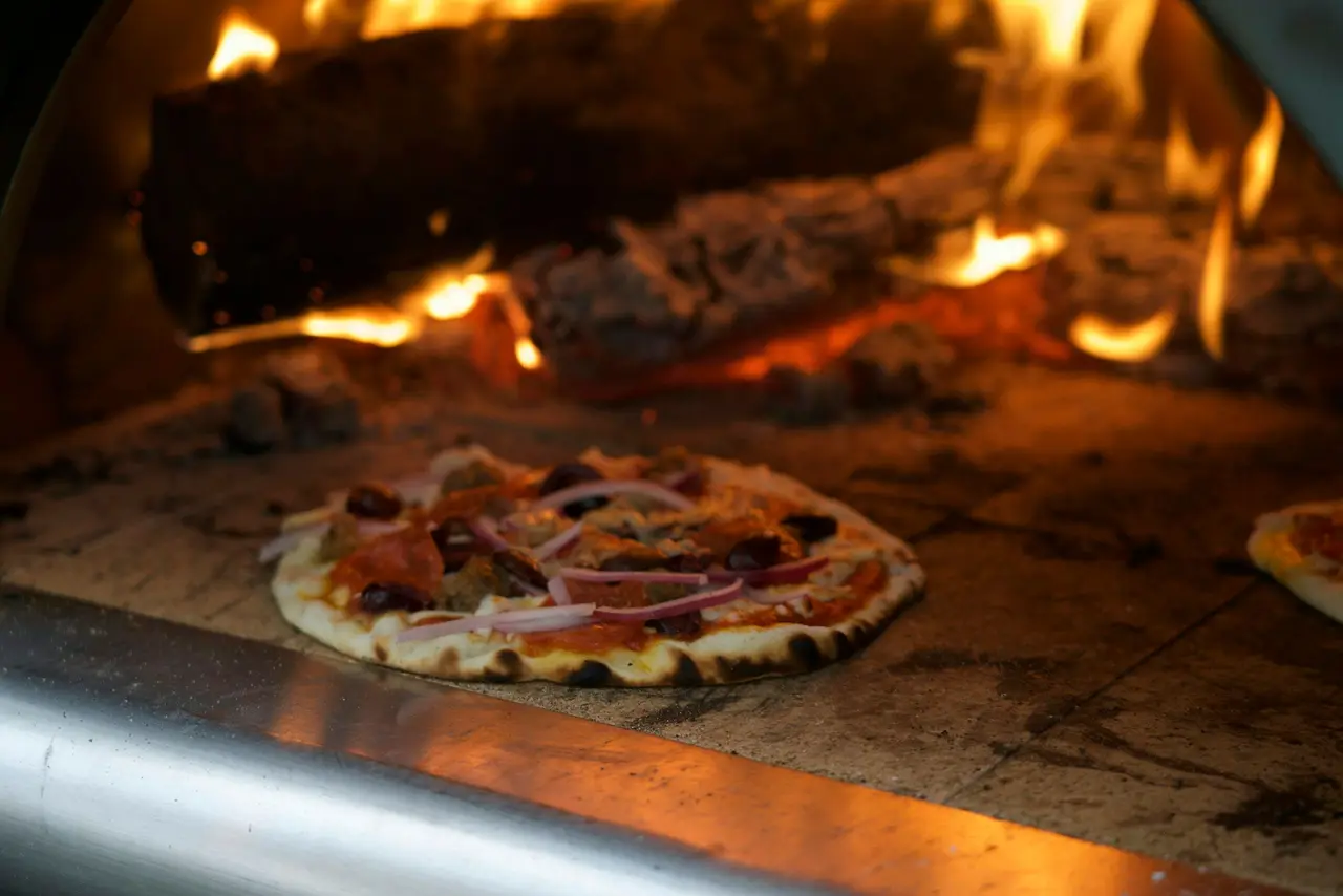 Une pizza cuit sur la sole du four, près des braises.