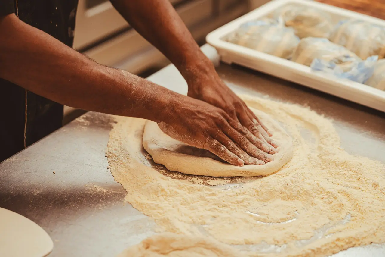 Des mains pétrissent la pâte sur un plan fariné.